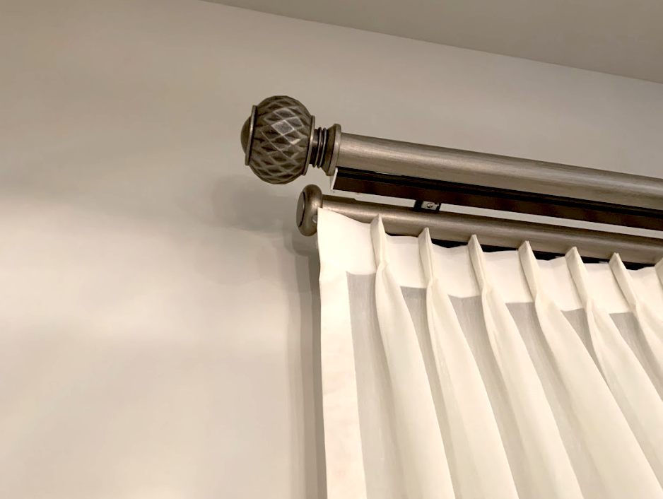 A curtain with pleats is hung from a metallic rod with decorative finials, elegantly dressing up the plain wall and transforming the ambiance.